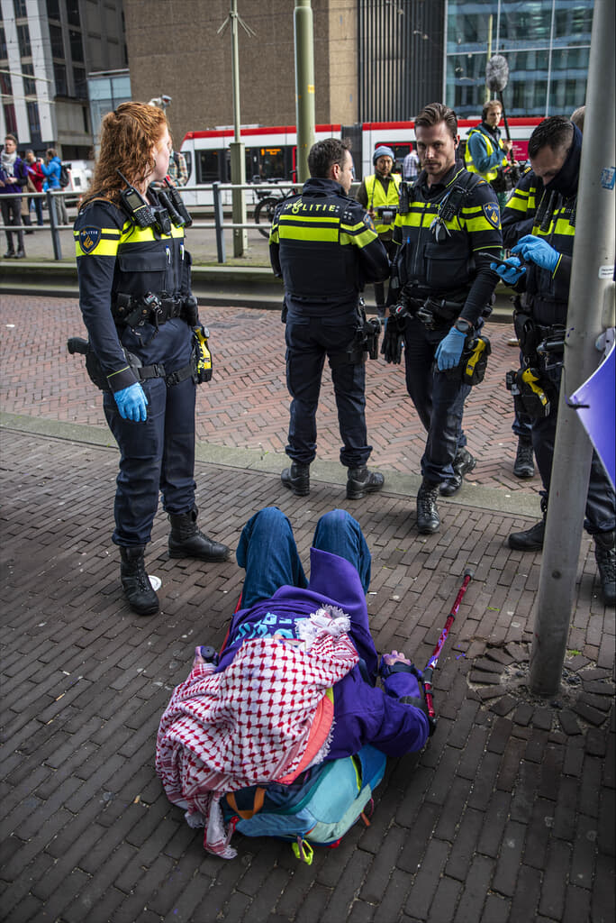 Rebel liggend op de grond met politieagenten er omheen.