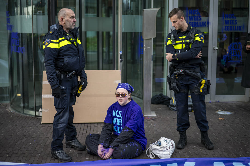 Rebel zittend op de grond met links en rechts een politieagent.
